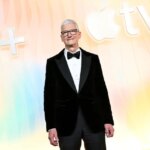 Мужчина в смокинге на фоне логотипа Apple TV+ на светлом фоне.