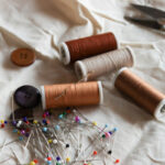 Катушка ниток, швейные булавки, пуговицы и ножницы на белоснежной ткани.