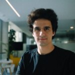 Мужчина в черной футболке в современном офисе с растительностью и большими окнами.