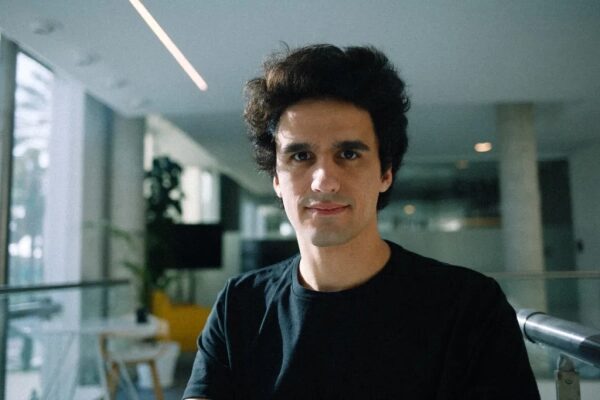 Мужчина в черной футболке в современном офисе с растительностью и большими окнами.