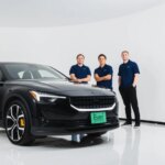 Черный автомобиль Polestar с сотрудниками в синей униформе на фоне белой стены.