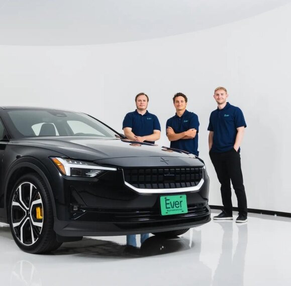 Черный автомобиль Polestar с сотрудниками в синей униформе на фоне белой стены.