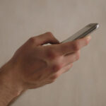 Рука держит смартфон, человек использует мобильное устройство для общения или работы.