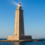 Старинный маяк на острове в море под голубым небом.