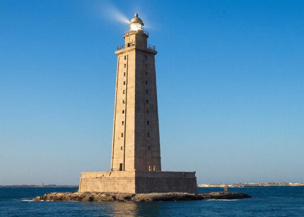Старинный маяк на острове в море под голубым небом.