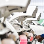 Рабочий проверяет автомобили на линии сборки, прозрачные капоты подняты.