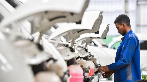 Почему электромобили набирают популярность в Африке 6 Рабочий проверяет автомобили на линии сборки, прозрачные капоты подняты.