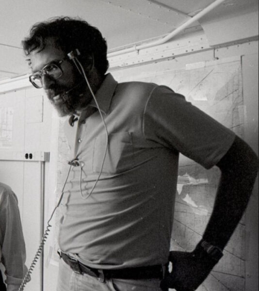 Мечта о машине со здравым смыслом 3 Человек в рубашке с гарнитурой разговаривает, стоя перед картой на стене.