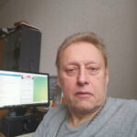 Человек в серой футболке в офисе рядом с компьютером.