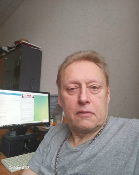 Человек в серой футболке в офисе рядом с компьютером.