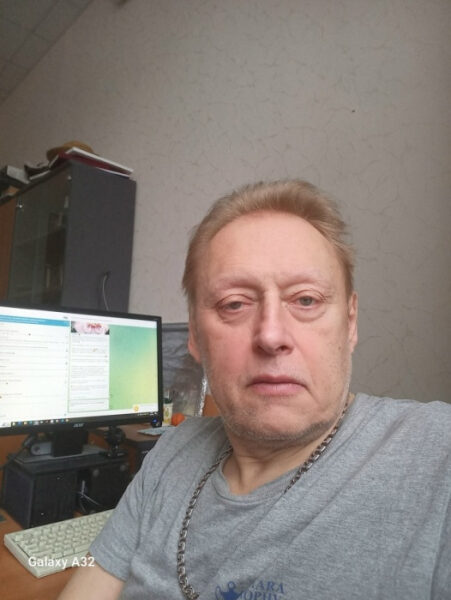 Человек в серой футболке в офисе рядом с компьютером.