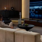 Человек смотрит гонки на большом экране в современной гостиной.