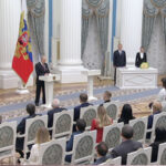 Церемония в Кремле: выступление перед аудиторией, государственные флаги, официальная обстановка.