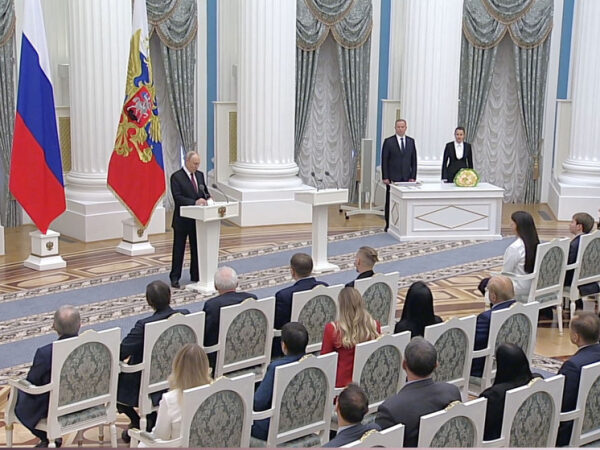 Церемония в Кремле: выступление перед аудиторией, государственные флаги, официальная обстановка.