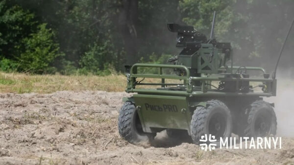Военный беспилотный наземный транспорт РЫСЬ PRO среди деревьев и песка.