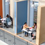 Современный офис, люди работают за столами в открытом пространстве с перегородками.