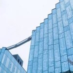 Современное стеклянное здание с текстовым узором на фасаде под серым небом.