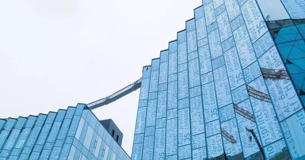 Современное стеклянное здание с текстовым узором на фасаде под серым небом.