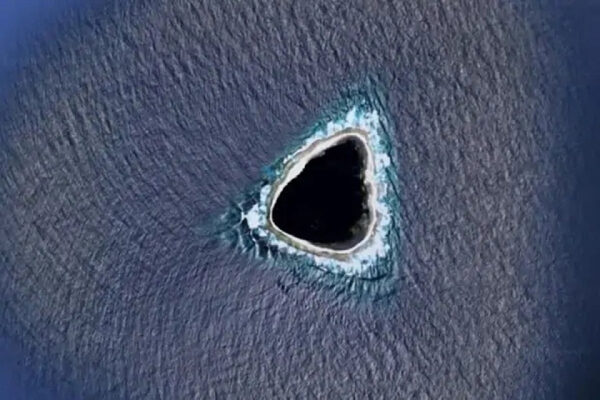 Треугольный остров в океане, окружённый темной водой и светлым берегом.