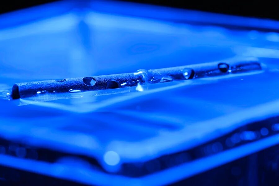 На поверхности плавает более длинная металлическая трубка с несколькими просверленными отверстиями из дистиллированной воды с голубым оттенком.