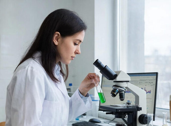 Женщина в лаборатории исследует жидкость в пробирке возле микроскопа.