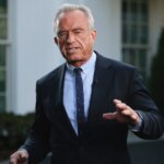 Мужчина в костюме и галстуке выступает на улице перед зданием.