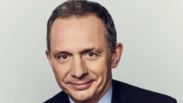 Мужчина в костюме с седыми волосами на светлом фоне, формальная деловая одежда.