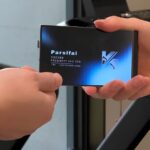 Обмен визитками: рука передаёт визитную карточку на фоне стеклянного окна.