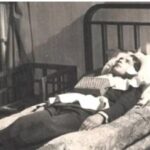 Человек в кровати, одет в костюм, с книгой на груди, комната в ретро-стиле.