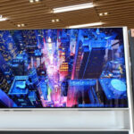 Телевизор LG OLED 8K с изображением города, представленный двумя людьми в шоуруме.