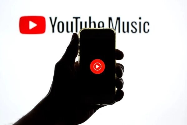 Рука с телефоном и логотипом YouTube Music на фоне экрана с логотипом YouTube Music.