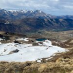 Горный пейзаж с заснеженными склонами и озером, вид сверху в ясный день.