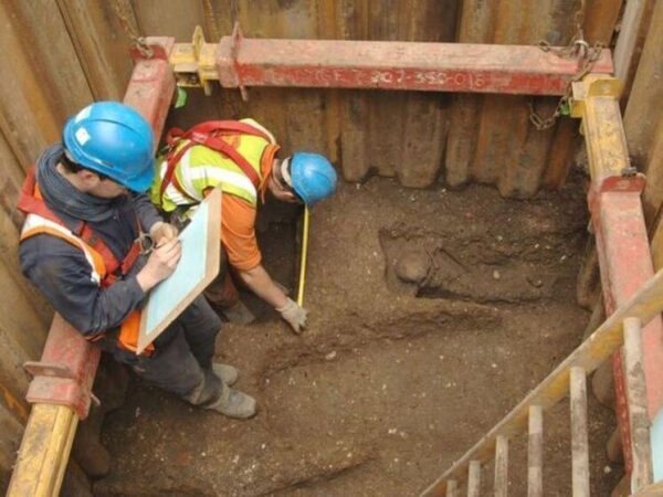 Археологи в касках исследуют раскопки с останками человека, делают записи.