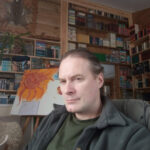 Мужчина в комнате с книжными полками, рядом картина с изображением подсолнуха.