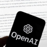 Смартфон с логотипом OpenAI на фоне текста на экране компьютера.