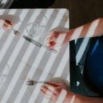 Люди за столом с приборами, солнечные полосы создают узор.