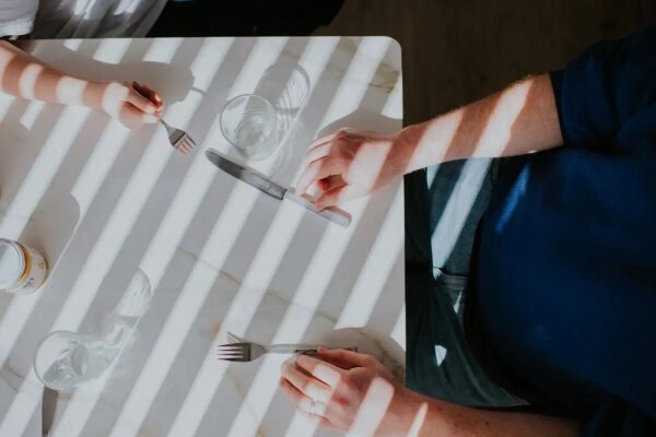 Люди за столом с приборами, солнечные полосы создают узор.