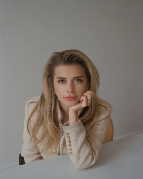 Блондинка в бежевом пиджаке за столом, светлый интерьер.