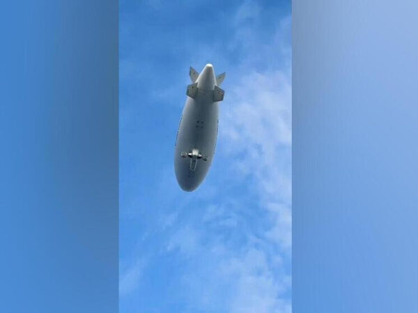 Дирижабль в голубом небе, вид снизу, летит высоко над облаками.