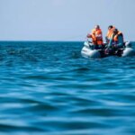 Двое рыбаков в лодке на синем море в оранжевых спасательных жилетах ловят рыбу.