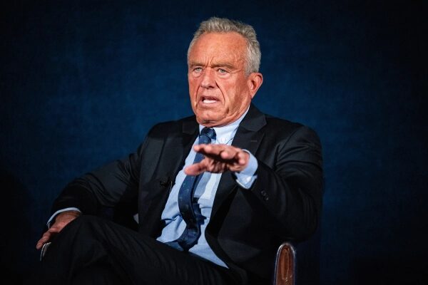 РФК-младший собрал на панельной дискуссии об аутизме чудаков и сторонников теорий заговора. 3 Мужчина в костюме сидит на стуле, жестом выделяя мысль, с серьезным выражением лица.