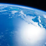 Вид на Землю из космоса, солнечные блики на океане, облака и голубой небосклон.