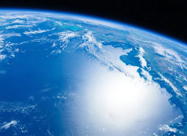 Загадка Земли: Почему наша планета пульсирует каждые 26 секунд? 5 Вид на Землю из космоса, солнечные блики на океане, облака и голубой небосклон.
