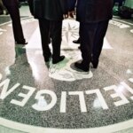 Люди стоят на мраморной эмблеме с буквами Центрального разведывательного управления.