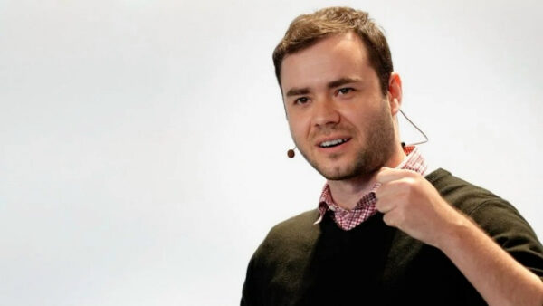 Мужчина выступает с микрофоном, жест выразительности, светлый фон.