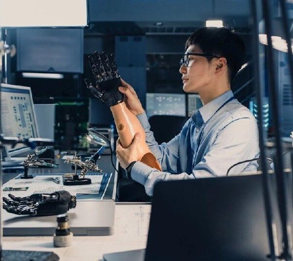 Инженер исследует протез в лаборатории, окруженной компьютерами и робототехникой.