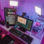 Игровое рабочее место с RGB-компьютером, двумя мониторами и аксессуарами, современное освещение.