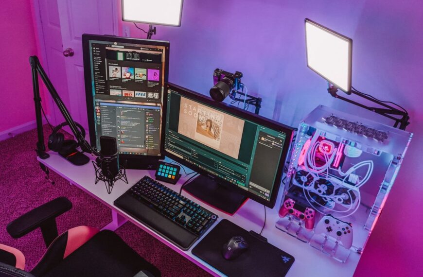 Игровое рабочее место с RGB-компьютером, двумя мониторами и аксессуарами, современное освещение.