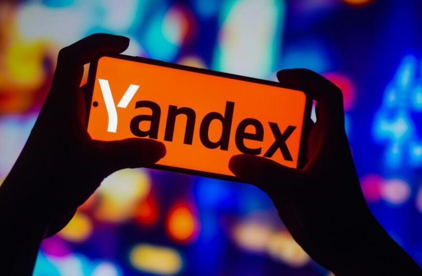 Смартфон с логотипом Яндекс на фоне ярких разноцветных огней.
