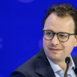 Мужчина в очках на фоне мероприятия, смотрит в сторону.